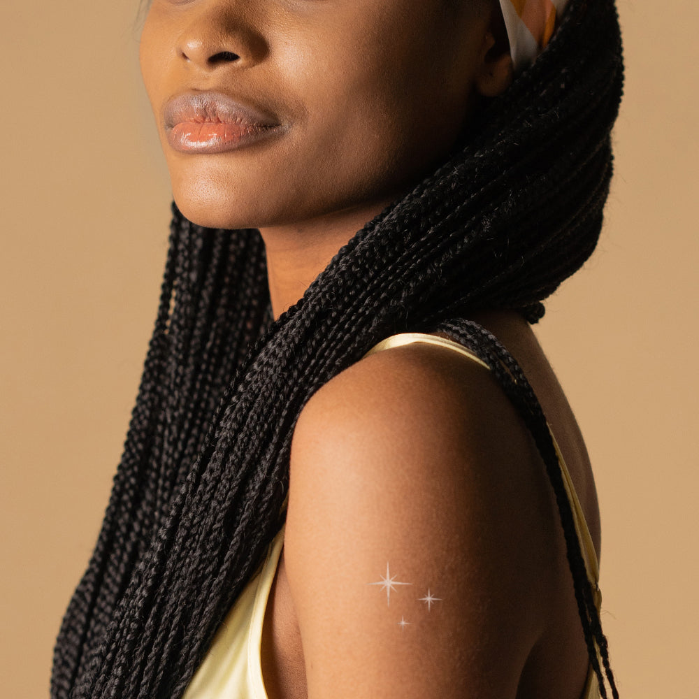 A woman's shoulder with 3 metallic silver twinkle stars on her skin